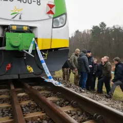 Grupa osób, w tym policjanci, ogląda przód lokomotywy EU07 005, otoczony taśmą policyjną.