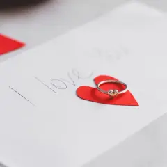 Pierścionek z serduszkiem na czerwonym sercu, obok napis "I love you". Idealne życzenia walentynkowe po angielsku.