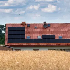 Dom z panelami słonecznymi na dachu, otoczony polami. Może to być znak, że nawet w spokojnej okolicy zdarzają się problemy z za wysokie napięcie w sieci.