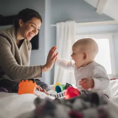 Radosne zabawy z 10 miesięcznym dzieckiem na łóżku. Mama i maluch dają sobie "piątkę".