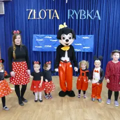 Dzieci i panie w strojach na dzień postaci z bajek, w tym Myszka Miki i Minnie, pozują do zdjęcia.