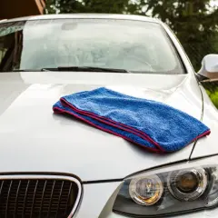 Niebieski ręcznik do osuszania auta leży na masce białego BMW. Idealny do rankingu najlepszych akcesoriów do pielęgnacji samochodu.
