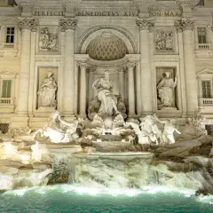 Trevi Fountain at night, with illuminated sculptures and cascading water.