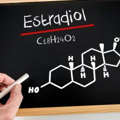 Tablica z napisem "Estradiol" i jego wzorem chemicznym C18H24O2. Dłoń trzyma kreda.