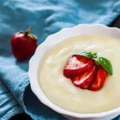 Gładka kaszka manna, czyli semolina co to, podana z truskawkami i miętą na niebieskim tle.
