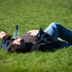 Mężczyzna leży na trawie obok butelki alkoholu, być może doświadczając skutków ubocznych po narkotykach, takich jak drgawki.