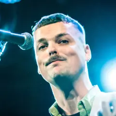 Blazej Krol śpiewa do mikrofonu, trzymając gitarę.