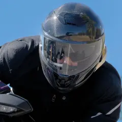 Motociclista con un casco mas silencioso de fibra de carbono, disfrutando del paisaje en un día soleado.