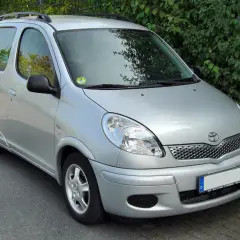 Srebrny Toyota Yaris Verso stoi na tle zielonych krzewów.