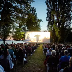 Open-air Kino in Boxberg: Viele Menschen sitzen auf Stühlen und schauen einen Film auf einer großen Leinwand am Seeufer.