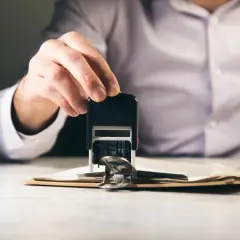 Dłoń z pieczątką nad dokumentami. Zastanawiasz się, ile czasu ma sąd na dostarczenie wyroku w sprawie cywilnej?