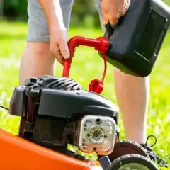 Osoba nalewa paliwo do kosiarki. Właściwe paliwo do kosiarki to klucz do jej sprawnego działania.