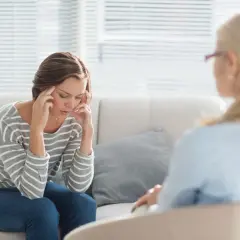 Kobieta z dłońmi na skroniach podczas sesji terapii behawioralnej.