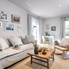 Gemütliches wohnzimmer grau blau holz mit großem Sofa, Holztisch und Schaukelstuhl. Bilder an der Wand und Fenster mit Vorhängen.