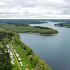 Vue aérienne d'un camping naturiste en Allemagne, bordé par une forêt dense et un lac paisible.