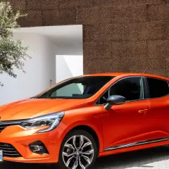 En orange Renault Clio 2026 parkerad vid en modern byggnad med en olivträd i förgrunden.