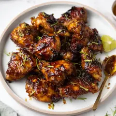 Krispiga kycklingvingar med en glansig glaze, garnerade med lime och örter. Ett perfekt recept för en smakrik glaze!
