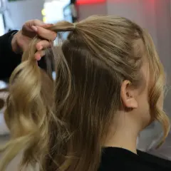 Tworzenie fryzury na Dzień Kobiet. Dłoń modeluje blond włosy, przygotowując je do stylizacji.