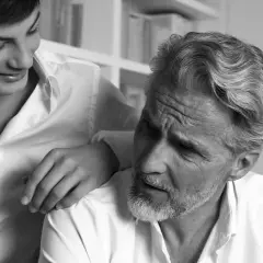 Un jeune homme pose sa main sur l'épaule d'un homme plus âgé, dont la barbe poil blanc est visible.