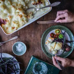 En härlig gratinerad blomkål i en ugnsform, serverad med färska grönsaker och en bok.