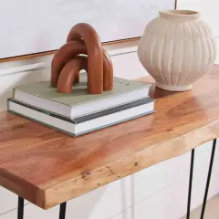 A live-edge acacia hardwood console table displays books, a wooden sculpture, and a textured vase.