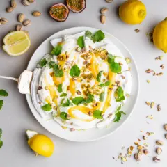 En vacker pavlova med lemoncurd, toppad med pistagenötter och mynta. Serveras med färska citroner och passionsfrukt.