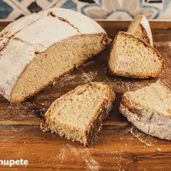 Un pan de papa casero, con su corteza dorada y miga esponjosa, cortado en rebanadas sobre una tabla de madera.
