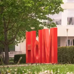 Große rote Buchstaben "HdM" vor einem Gebäude. Hier könnte dein berufsbegleitendes Studium in Stuttgart beginnen.