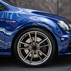 Błyszczące, niebieskie auto z felgami aluminiowymi. Widok z boku na przednie koło, idealny moment dokręcania kół aluminiowych.