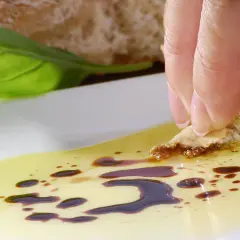 Ein Stück Brot wird in Olivenöl mit Balsamico getunkt. Eine Frau genießt diesen Snack, vielleicht während der Schwangerschaft.