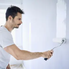Mann streicht Wand mit weißer Farbe. Die Nachteile von Latexfarbe sind, dass sie schwer zu entfernen ist.