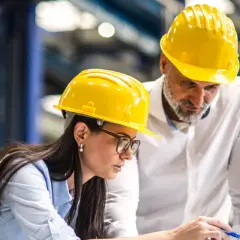 Zwei Ingenieure, ein Mann und eine Frau, mit gelben Schutzhelmen arbeiten an einem Laptop.