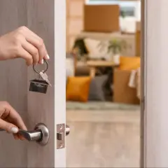Manos abren la puerta con llaves de casa, un gran tenedor cuelga del llavero. El interior está lleno de cajas de mudanza.