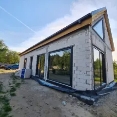 Nowy dom w stanie surowym zamkniętym, z dużymi oknami i dachem.