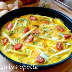 Omelette aux asperges vertes et oignons, garnie de tomates cerises, prête à être dégustée. Une recette simple et savoureuse.