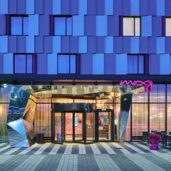 Nowoczesny budynek Moxy Hotels Pyrzowice nocą, z niebieską fasadą i neonowym logo.