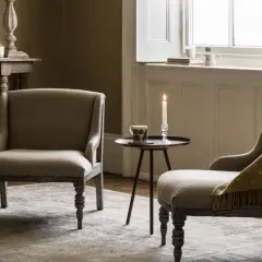 Dwa fotele w stylu angielskim, przytulny kącik z kocem i świecą, tworzą ciepłą atmosferę.