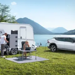 Para wakacyjna z przyczepą kempingową i ładowanym autem elektrycznym nad jeziorem. Idealne na wycieczkę z prawem jazdy B96.