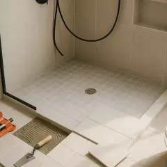 Outils pour installer une douche italienne : carreleur, truelle, seau de mortier. La pose des carreaux est en cours.
