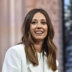 Izabella Krzan w białej marynarce, uśmiechnięta, z mikrofonem przy uchu.