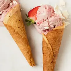 Zwei Waffelhörnchen mit cremigem Erdbeereis und zerbrochenem Baiser.