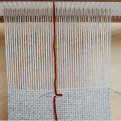 Début d'un tissage sur métier, fils de coton gris et rouge. La technique de tissage se révèle avec chaque passage.