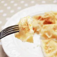 Widok z bliska na widelec z pierogiem z serem, posypanym cynamonem. Na talerzu widać więcej pysznych pierogów.