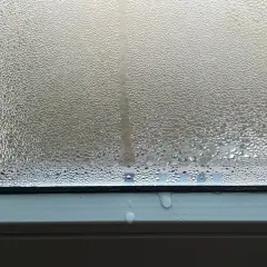 Goccioline d'acqua su un vetro, un fenomeno che illustra il concetto di traspirante significato, con condensa che scivola sul davanzale.
