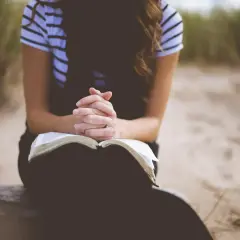 Kobieta z dłońmi złożonymi nad otwartą Biblią, w ciszy szuka siły i spokoju. To jej modlitwa o dobry dzień w pracy.