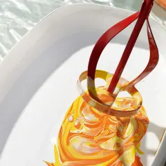 Ein roter Rührer mischt leuchtend gelbe und orangefarbene Wandfarbe in einem weißen Eimer.