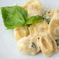 Pyszne ravioli w kremowym sosie, posypane parmezanem i udekorowane listkiem bazylii. Idealne danie, które podpowiada, ravioli z czym podawać.