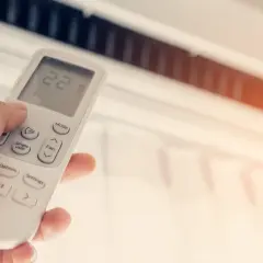 Mano ajustando el control remoto del aire acondicionado, mostrando la temperatura a 22 grados. ¿Qué potencia de aire acondicionado necesito para mi hogar?