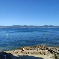 Vista desde punta Faxilda. El mar azul se extiende hasta la costa montañosa, con un kayak solitario y boyas amarillas.
