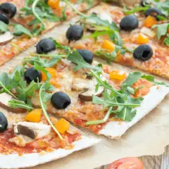 Eine leckere vollkorn pizza mit Pilzen, Oliven und Rucola, belegt mit geschmolzenem Käse und Paprikawürfeln.